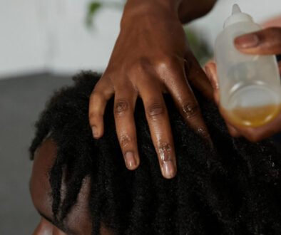 Young black man with locs gets his hair oiled by friend whilst sitting on the bedroom floor